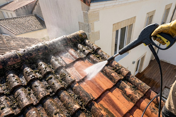 Artisan couvreur équipé d'un harnais de sécurité projetant de l'eau sous haute pression pour éliminer la mousse épaisse sur des tuiles