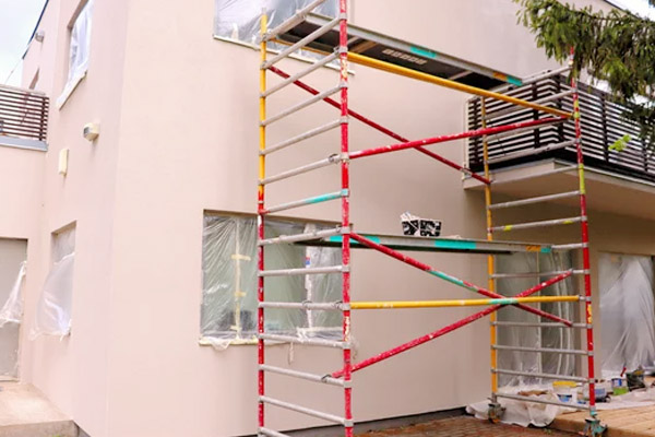 Façade de maison en cours de ravalement avec un échafaudage tubulaire installé et fenêtres protégées par des bâches